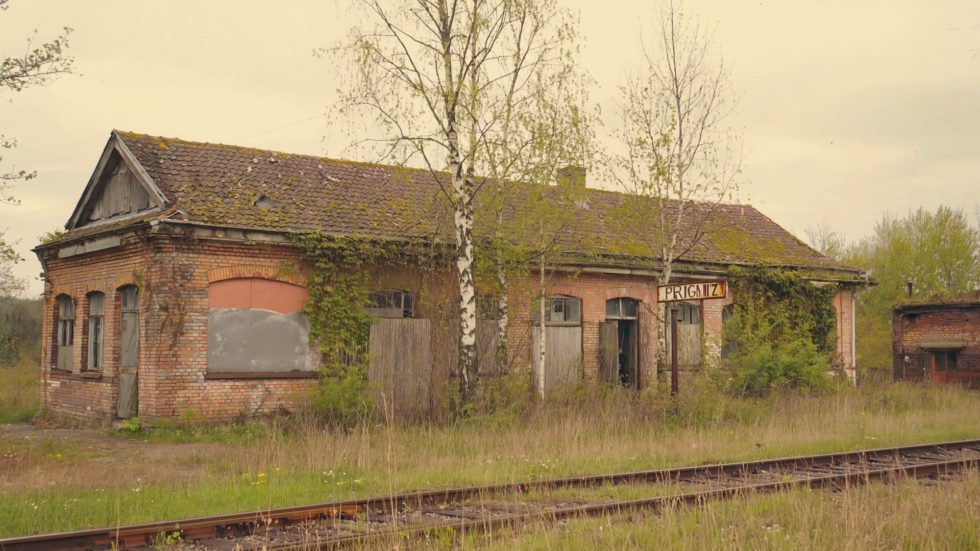 Verlassene Bahnhofsfassade aus Backstein mit überwachsenem Bahnsteig und Efeu